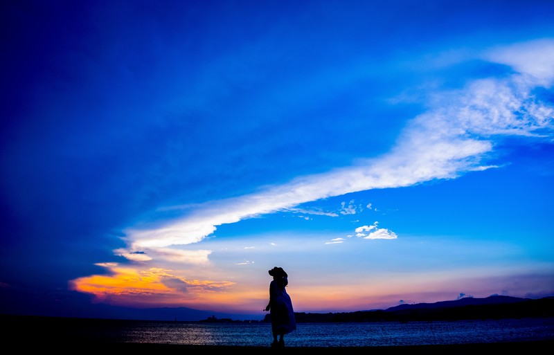 夕焼けの海に散歩する女性の写真